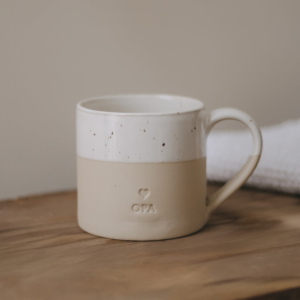 Eine große Tasse aus Keramit mit der Prägung "Opa" steht auf einem Holztisch.