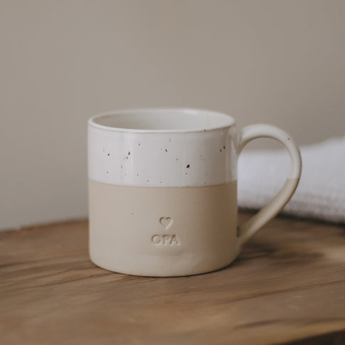 Eine große Tasse aus Keramit mit der Prägung "Opa" steht auf einem Holztisch.