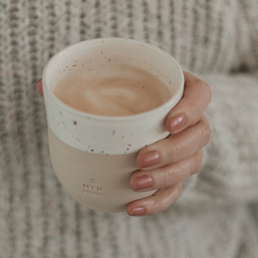 Warmer Kaffee in Becher „Let it Snow“, gehalten von einer Hand