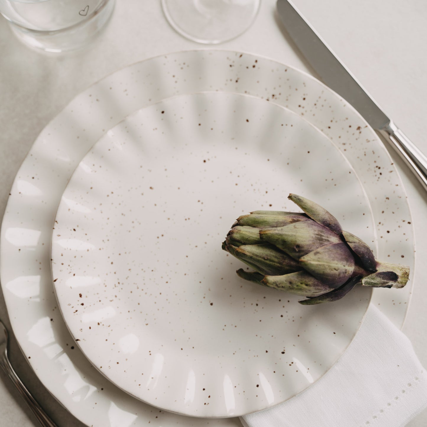 Colina-Teller auf gedecktem Tisch mit Artischocke und Besteck, mediterrane Stimmung