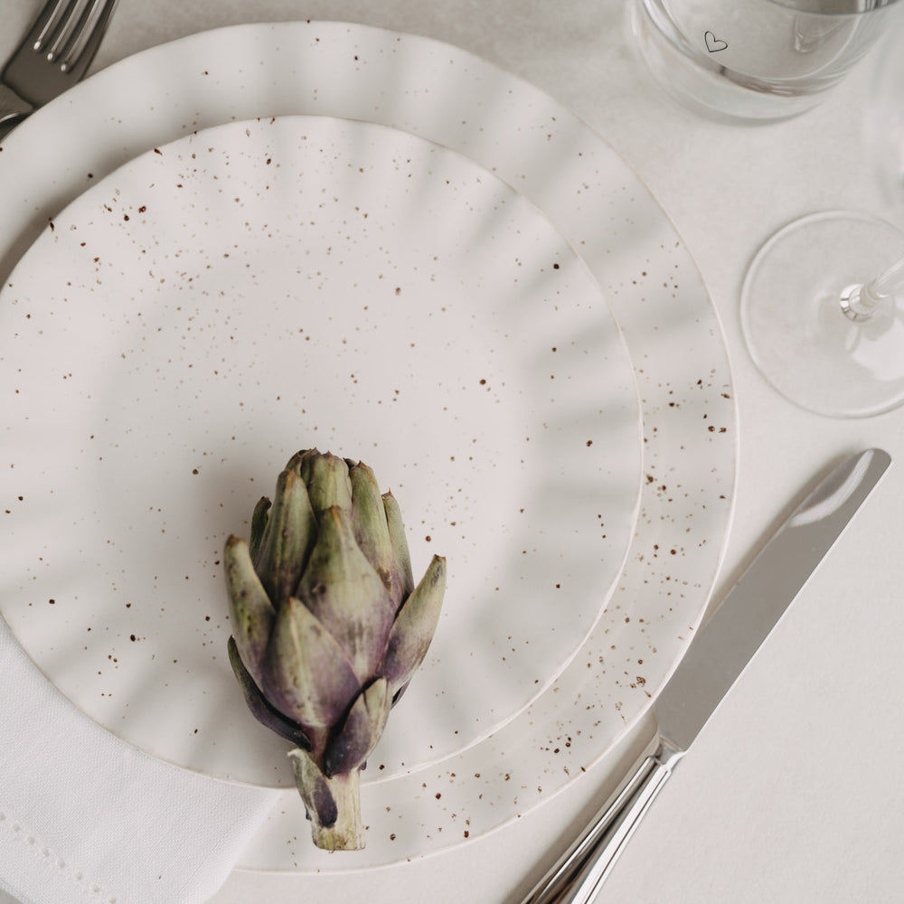 Colina-Teller auf gedecktem Tisch mit Artischocke und Besteck, mediterrane Stimmung
