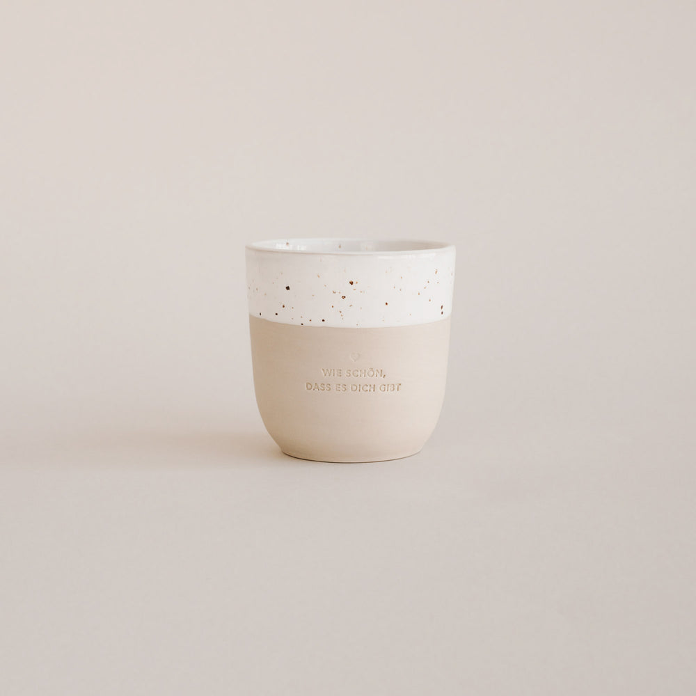 Auf einem grauen Hintergrund steht ein handgetöpfter Becher mit der Prägung "Wie schön, dass es dich gibt."