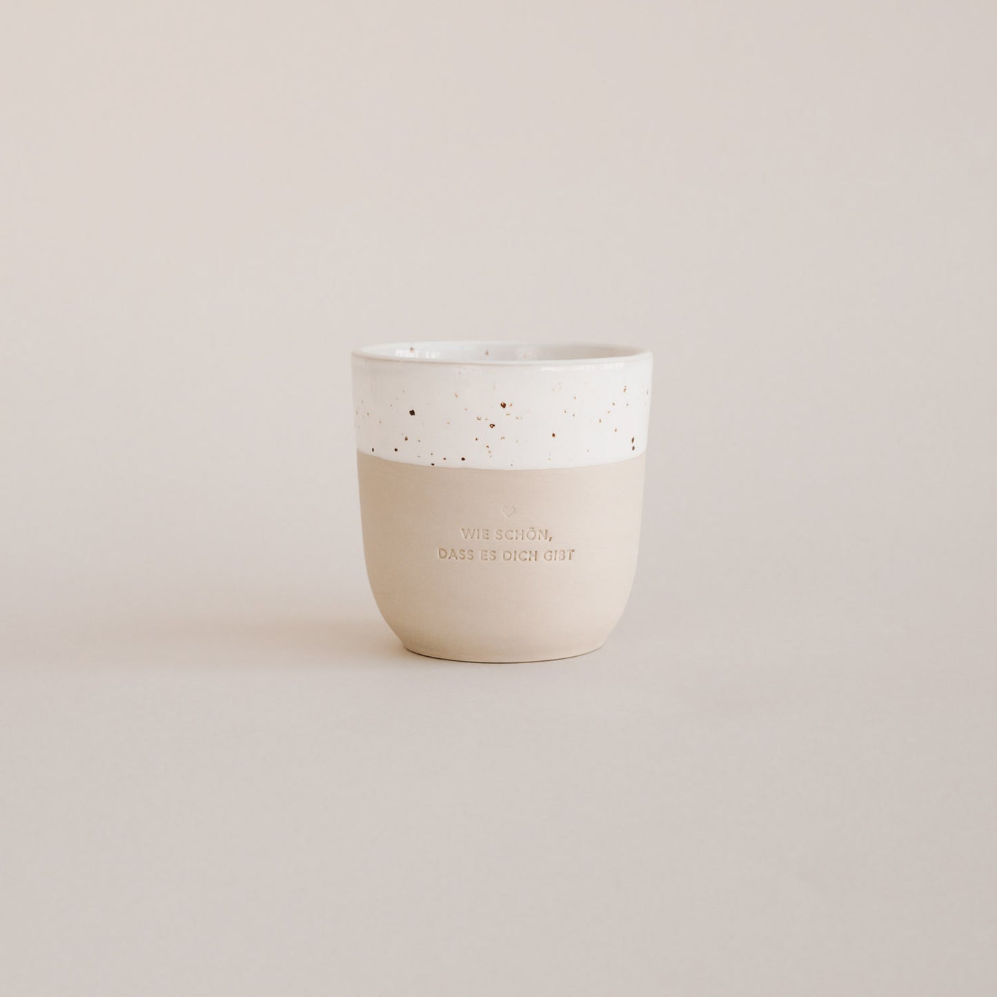 Auf einem grauen Hintergrund steht ein handgetöpfter Becher mit der Prägung "Wie schön, dass es dich gibt."