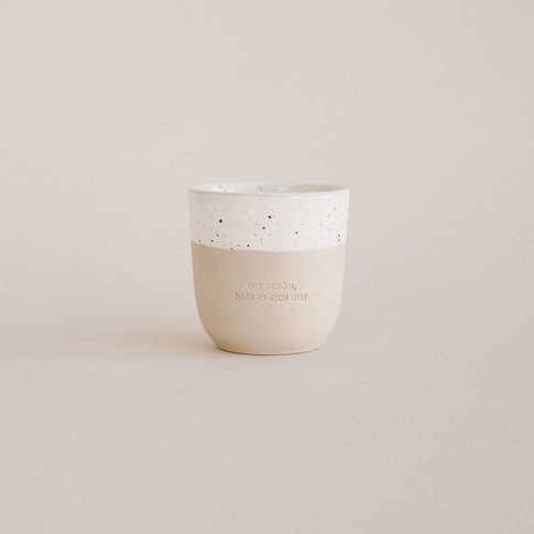 Auf einem grauen Hintergrund steht ein handgetöpfter Becher mit der Prägung "Wie schön, dass es dich gibt."