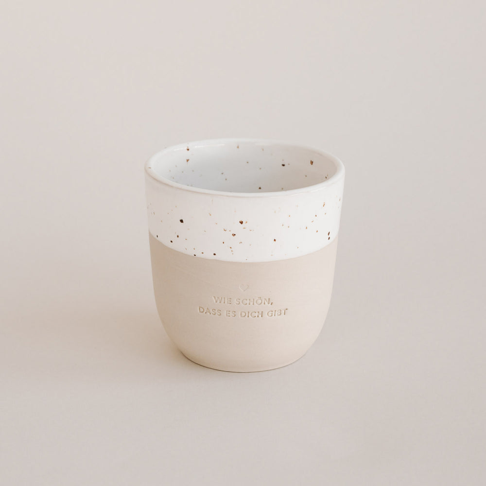 Auf einem grauen Hintergrund steht ein handgetöpfter Becher mit der Prägung "Wie schön, dass es dich gibt."