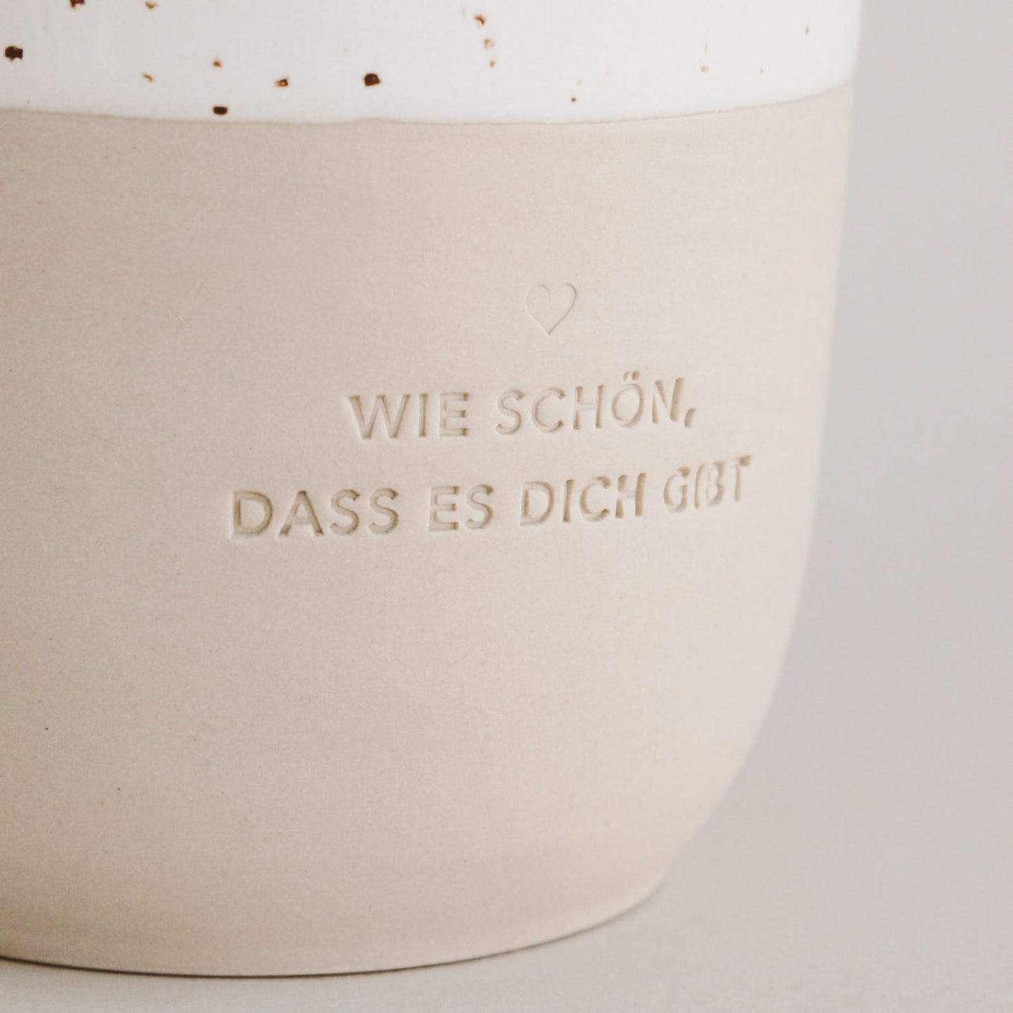 Nachaufnahme von der Prägung "Wie schön, dass es dich gibt" auf einem Steingut Becher.