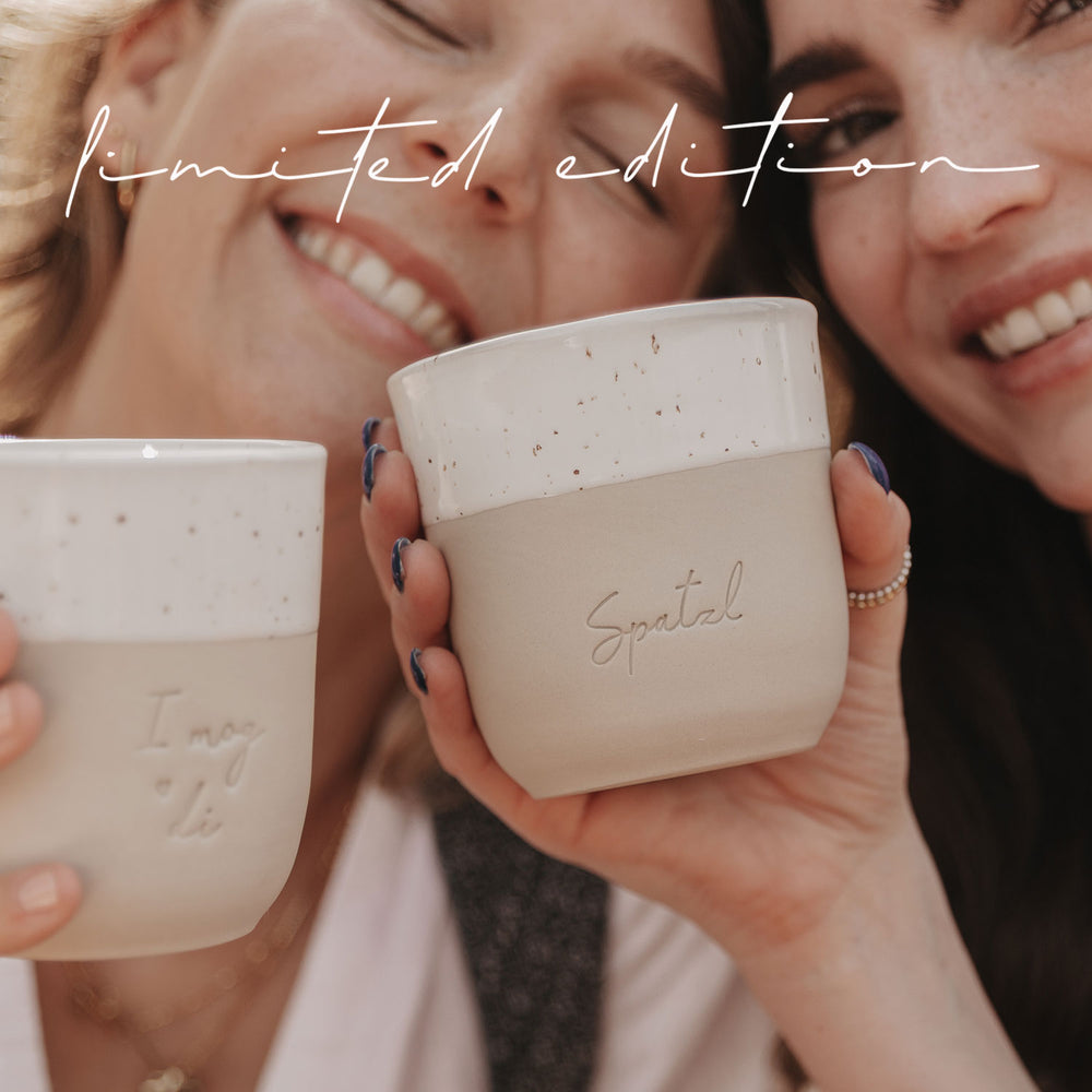 Nahaufnahme von zwei Frauen, die die limitierten Becher „I mog di“ und „Spatzl“ in der Hand halten.