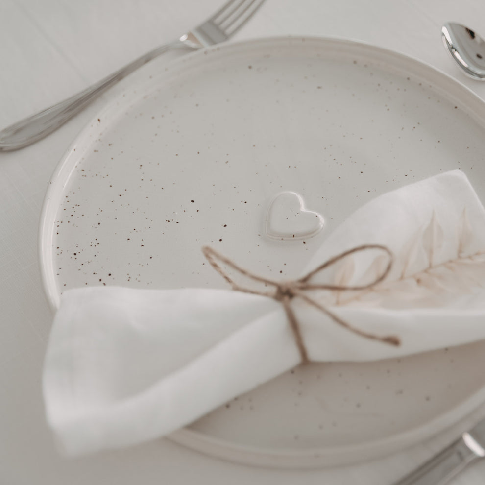 Calma Speiseteller mit Herzprägung auf festlich gedecktem Tisch mit Stoffserviette und Besteck