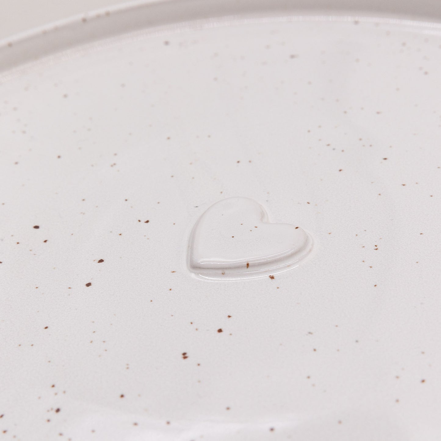 Herzdetail des Calma Speisetellers in Cremeweiß mit feinen Sprenkeln und erhabener Prägung
