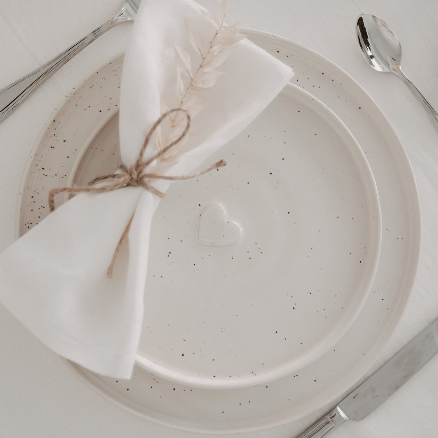 Zwei Calma Frühstücksteller aus Keramik mit Herzprägung, dekoriert mit Stoffserviette und Besteck auf weißem Tisch.