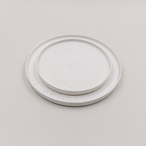 Zwei übereinandergelegte Calma Teller in unterschiedlichen Größen mit Herzprägung auf hellem Hintergrund.