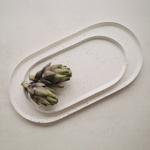 Servierplatten Calma in zwei Größen auf hellem Tisch – Detail mit Artischocken als Deko