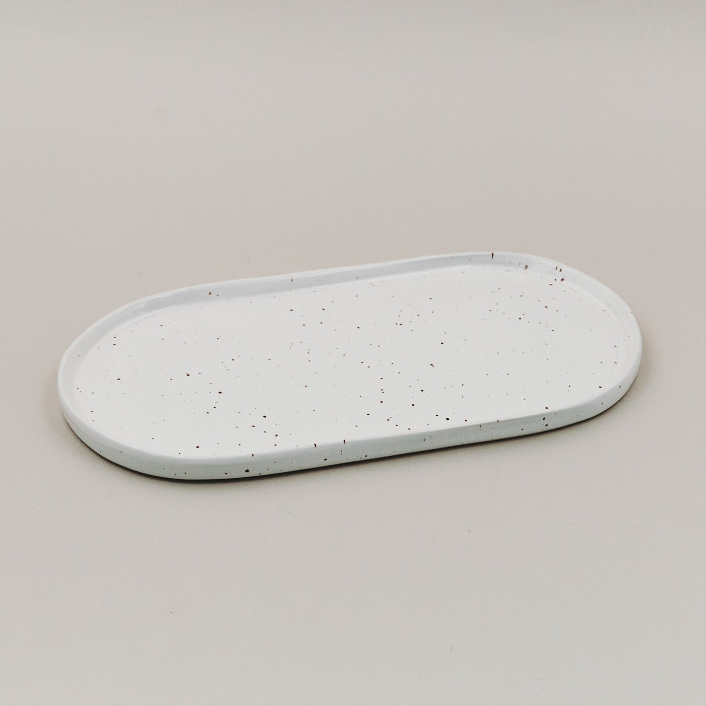 Servierplatte Calma klein aus weißem Steingut mit Sprenkelmuster auf hellem Untergrund