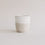 Keramikbecher in Beige und Weiß mit drei Herzprägungen, minimalistisch fotografiert vor hellem Hintergrund.