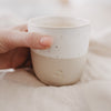 Beige-weißer Keramikbecher mit Herzprägung wird in der Hand gehalten – detailreiche Nahaufnahme.