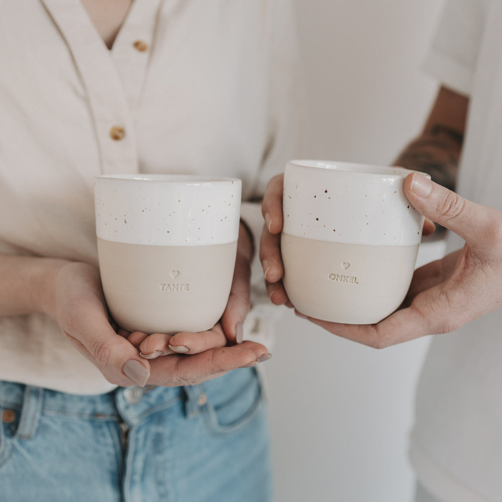 Zwei Personen halten Keramikbecher TANTE und ONKEL in Beige-Weiß mit Speckle-Optik von Eulenschnitt.