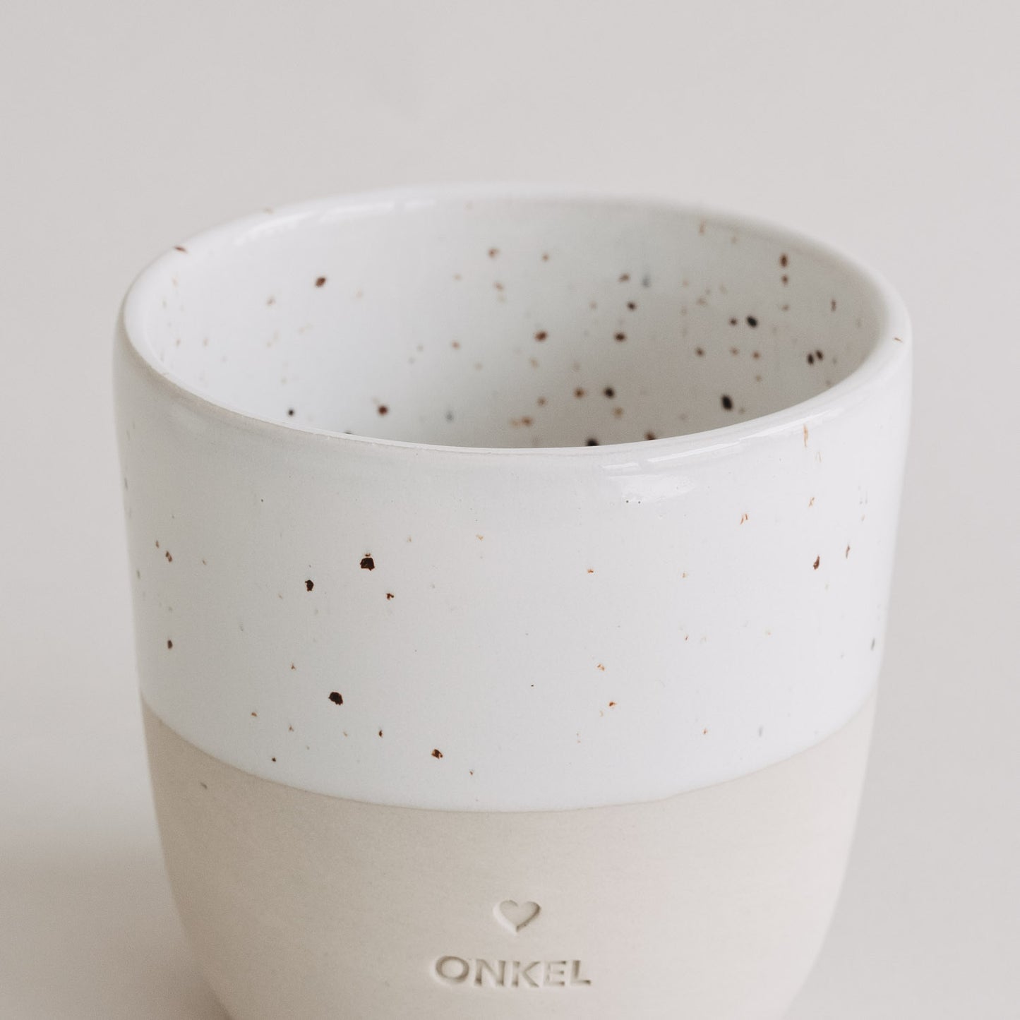 Nahaufnahme des Keramikbechers „Onkel“ mit weißer, gesprenkelter Glasur und matter beiger Unterseite.