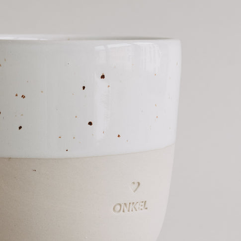 Detailaufnahme des Bechers „Onkel“ mit Herzprägung und zweifarbiger Keramikoberfläche in Beige und Weiß.