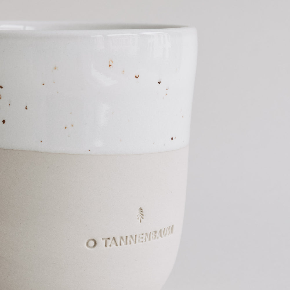 Detailaufnahme des Keramikbechers „O Tannenbaum“ mit weißer Sprenkelglasur und beige-matter Unterseite.