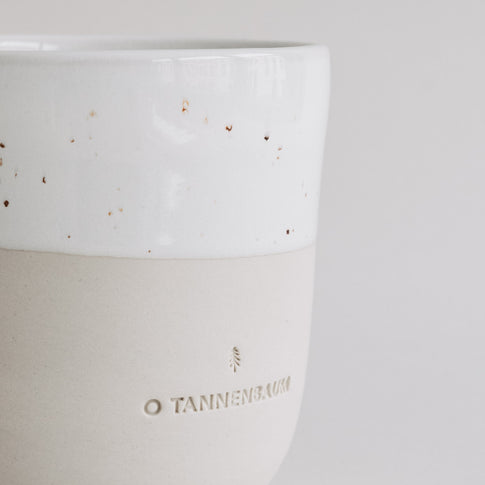 Detailaufnahme des Keramikbechers „O Tannenbaum“ mit weißer Sprenkelglasur und beige-matter Unterseite.