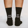 Nahaufnahme von zwei Beinen in schwarzen Socken mit weißer Schrift. Auf der linken Socke steht 'DER BODEN', auf der rechten 'IST LAVA'.