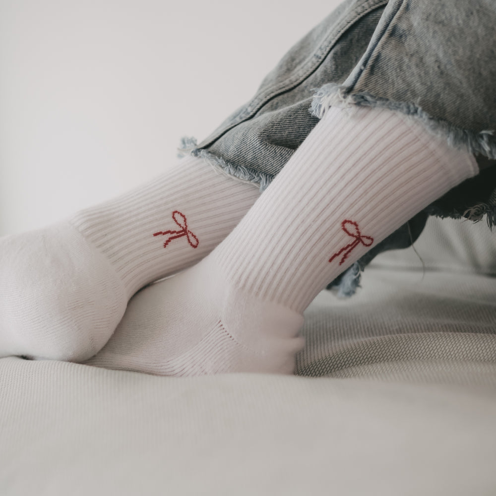 Nahaufnahme von Beinen in hochgekrempelten Jeans, die weiße Socken mit roter Schleifen-Motiv auf der Ferse tragen.