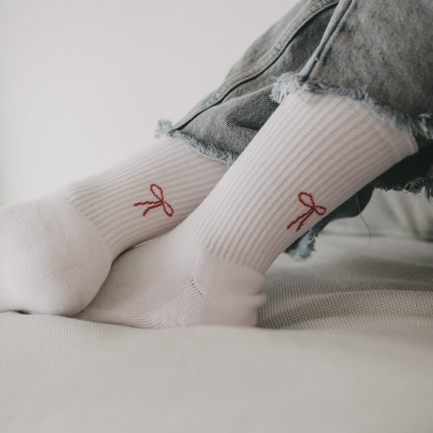 Nahaufnahme von Beinen in hochgekrempelten Jeans, die weiße Socken mit roter Schleifen-Motiv auf der Ferse tragen.