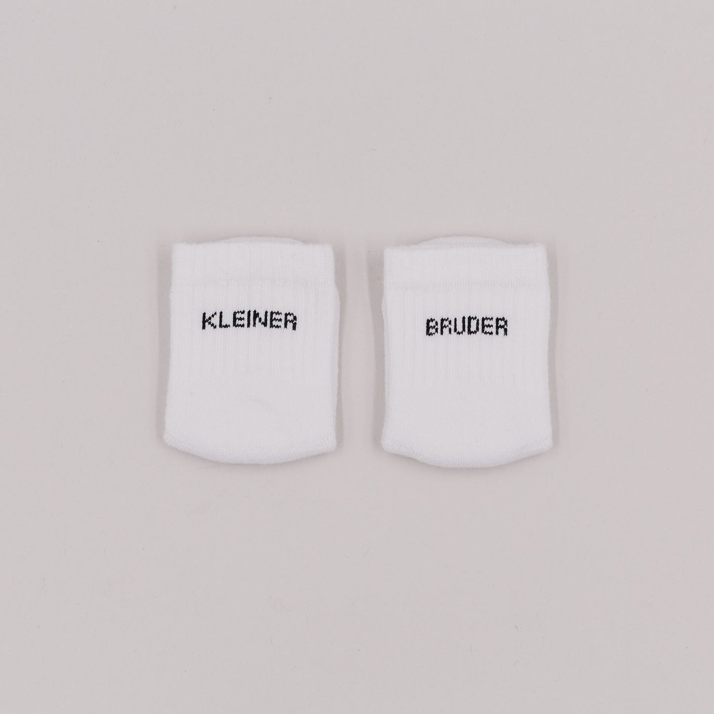 Weiße Babysocken mit Schriftzug „Kleiner Bruder“ auf neutralem Hintergrund