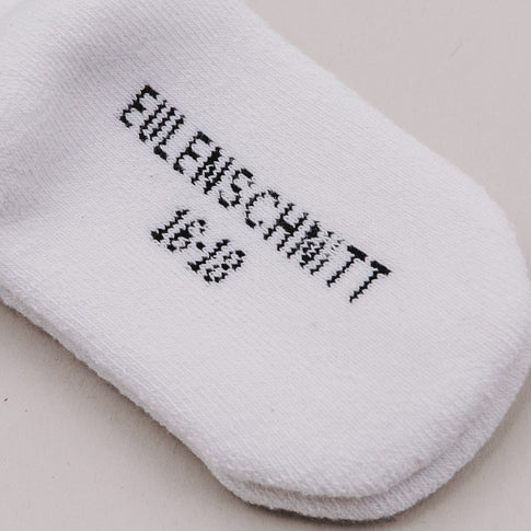 Nahaufnahme der Sohle einer weißen Babysocke mit dem Schriftzug „Eulenschnitt 16/18“.