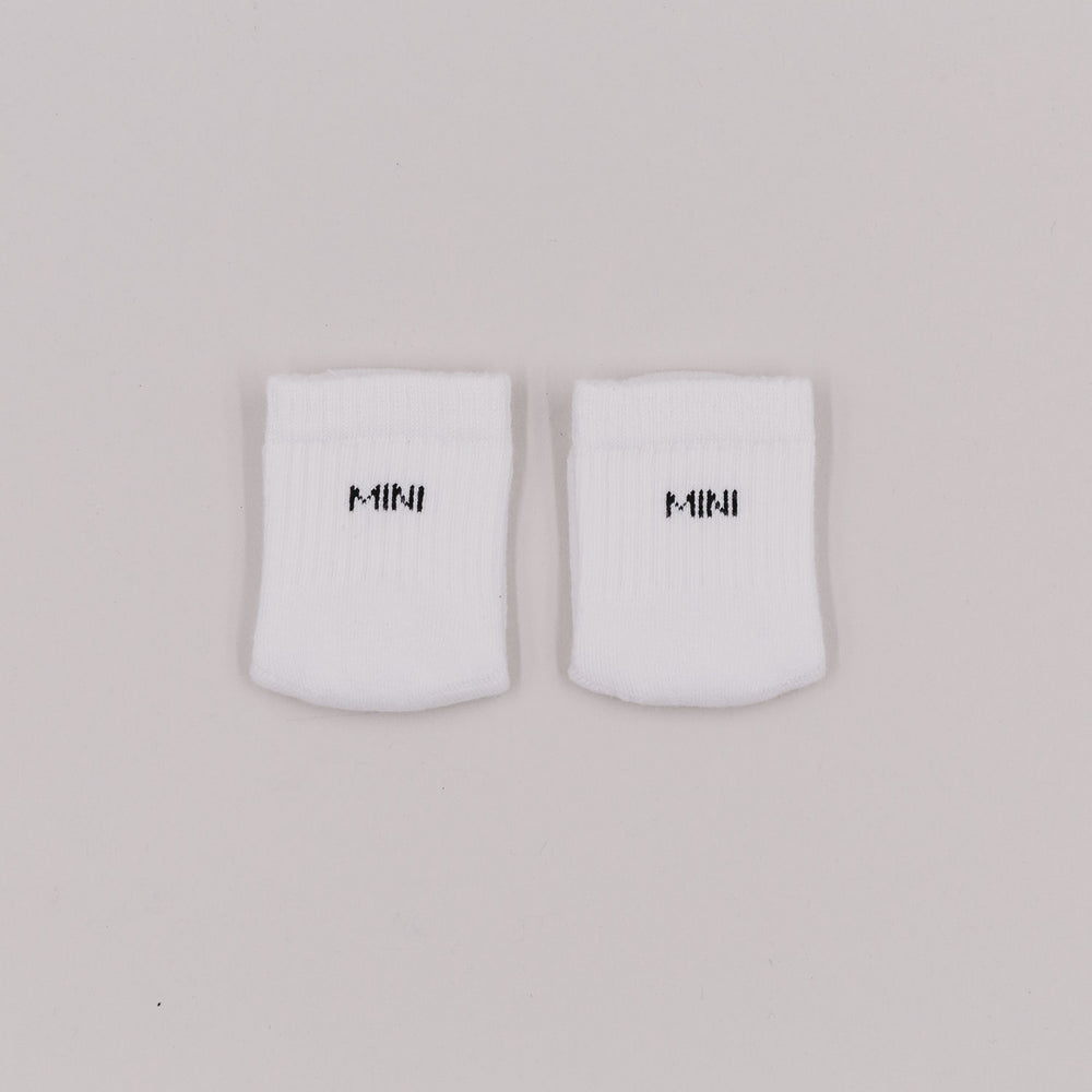 Weiße Babysocken mit schwarzer „MINI“-Stickerei auf hellem Untergrund, flach nebeneinandergelegt