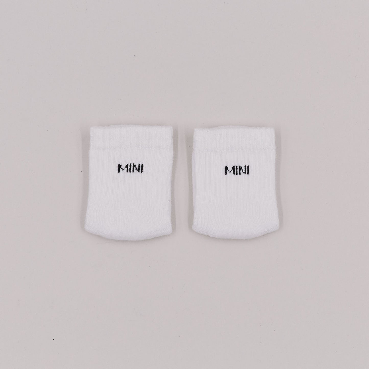 Weiße Babysocken mit schwarzer „MINI“-Stickerei auf hellem Untergrund, flach nebeneinandergelegt