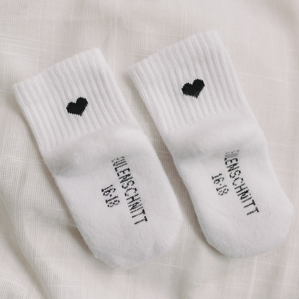 Detailaufnahme von Babysocken mit schwarzem Herz und Eulenschnitt-Schriftzug auf der Fußsohle.