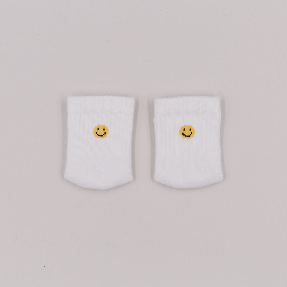 Zwei weiße Babysocken mit gelbem Smiley-Stick auf hellem Hintergrund, von oben fotografiert.
