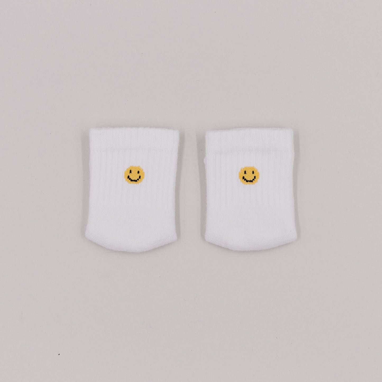 Zwei weiße Babysocken mit gelbem Smiley-Stick auf hellem Hintergrund, von oben fotografiert.