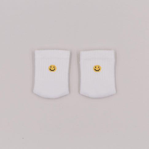 Zwei weiße Babysocken mit gelbem Smiley-Stick auf hellem Hintergrund, von oben fotografiert.