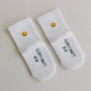 Weiße Babysocken mit gelbem Smiley und Eulenschnitt-Schriftzug auf glattem, hellem Hintergrund.