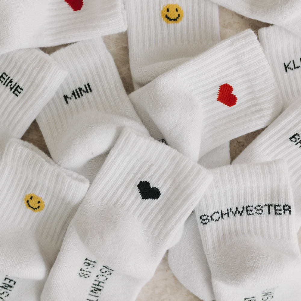 Detailansicht verschiedener Babysocken mit Stickereien wie Herz, Smiley, Bruder und Mini.