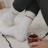 Person in weißen „Team Glühwein“-Socken sitzt mit einem Glas Glühwein auf einem hellen Teppich.