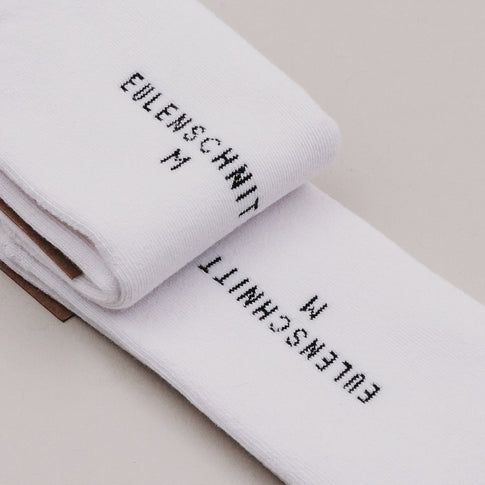 Nahaufnahme der zusammengelegten Socken mit „Eulenschnitt M“-Label in schwarzer Schrift auf weißem Stoff.