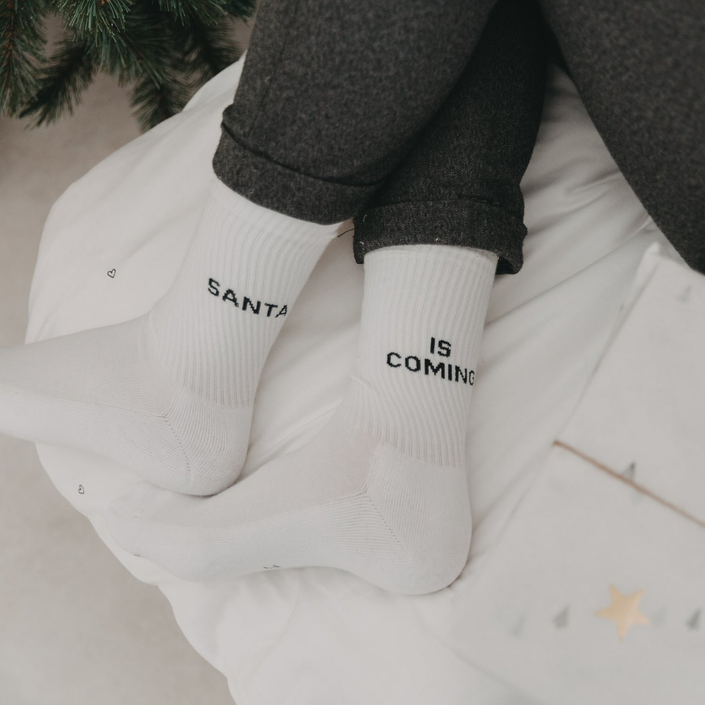 „Santa is coming“-Socken an gemütlich ausgestreckten Füßen auf Bettdecke mit Weihnachtsdeko