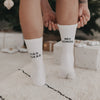Person trägt Ciao Kakao mit Schuss Socken vor dem Weihnachtsbaum, Schrift sichtbar an den Waden
