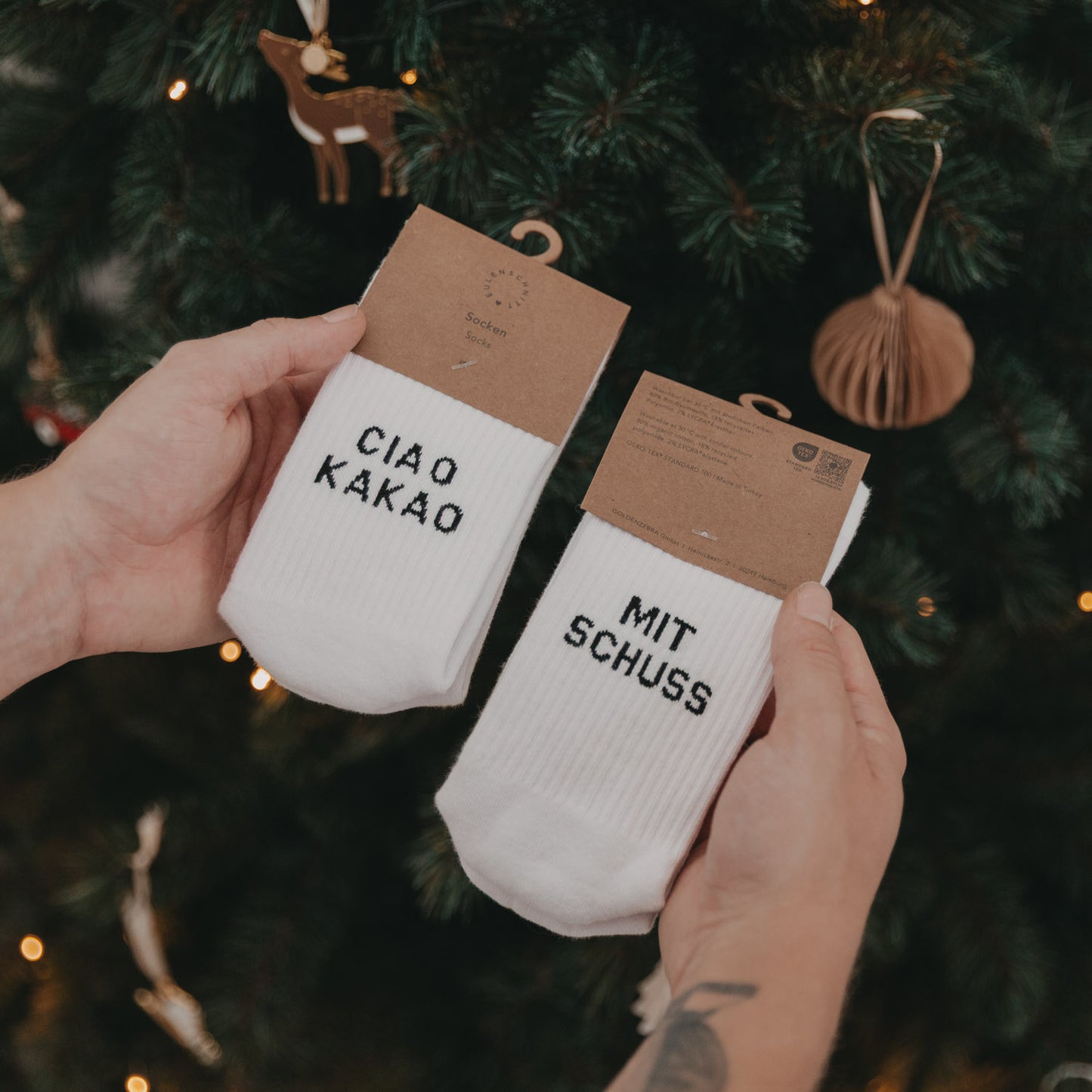 Ciao Kakao mit Schuss Socken in Verpackung, vor einem geschmückten Weihnachtsbaum präsentiert