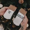 Socken „Meet me“ und „Under the mistletoe“ in Verpackung vor einem dekorierten Weihnachtsbaum in Händen gehalten