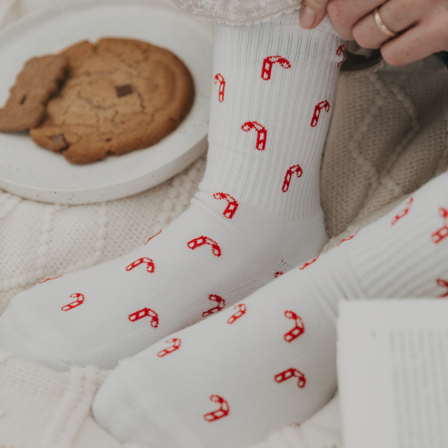 Zuckerstangen-Socken an Füßen mit Teller voller Plätzchen – weihnachtlicher Wohlfühlmoment.