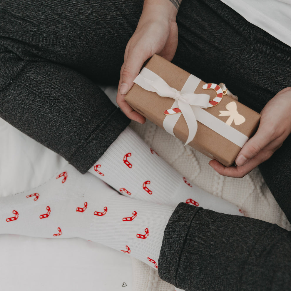 Schenkmoment mit Zuckerstangen-Socken und Geschenk in der Hand – perfekte Geschenkidee zu Weihnachten.