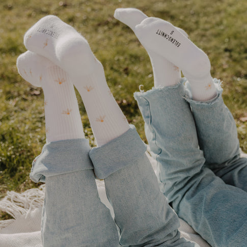 Zwei Personen tragen weiße Socken mit Gänseblümchen-Muster im natürlichen Outdoor-Look