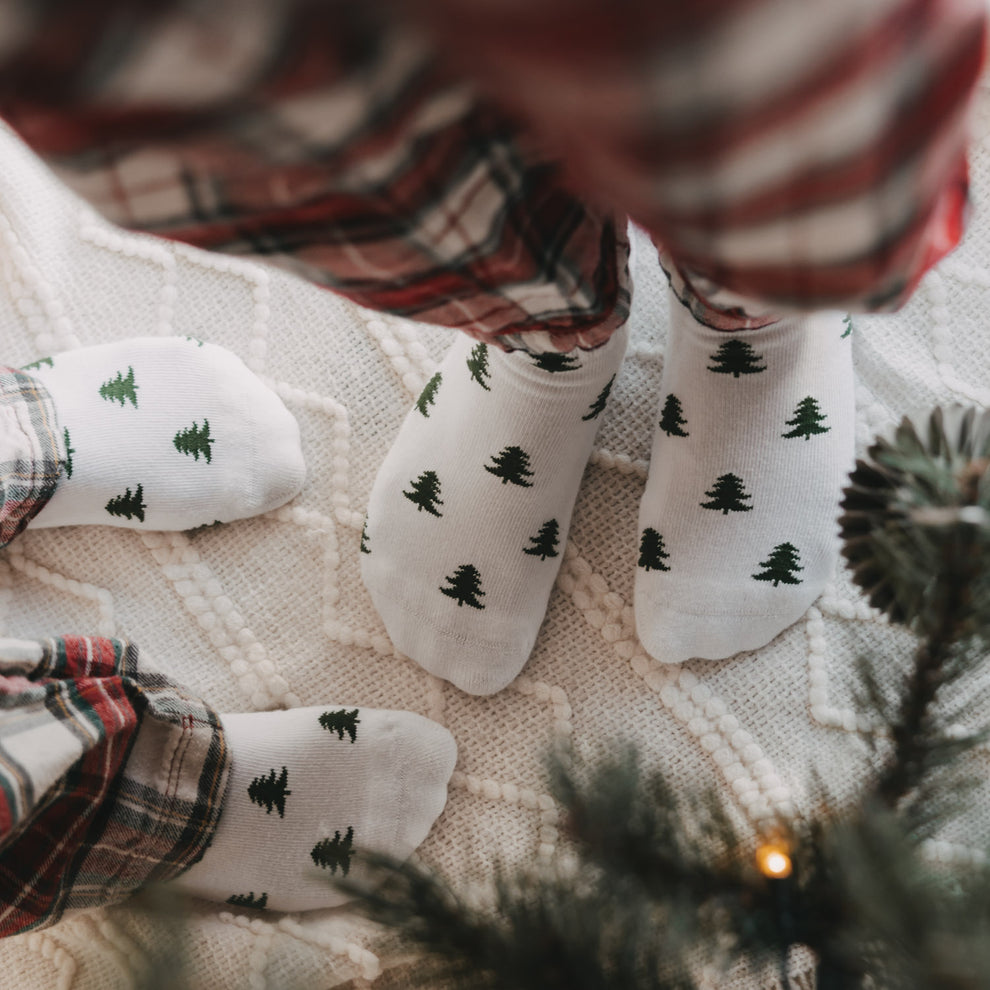 Weiße Eulenschnitt Socken mit grünen Tannen für Erwachsene und Kinder in weihnachtlicher Atmosphäre.
