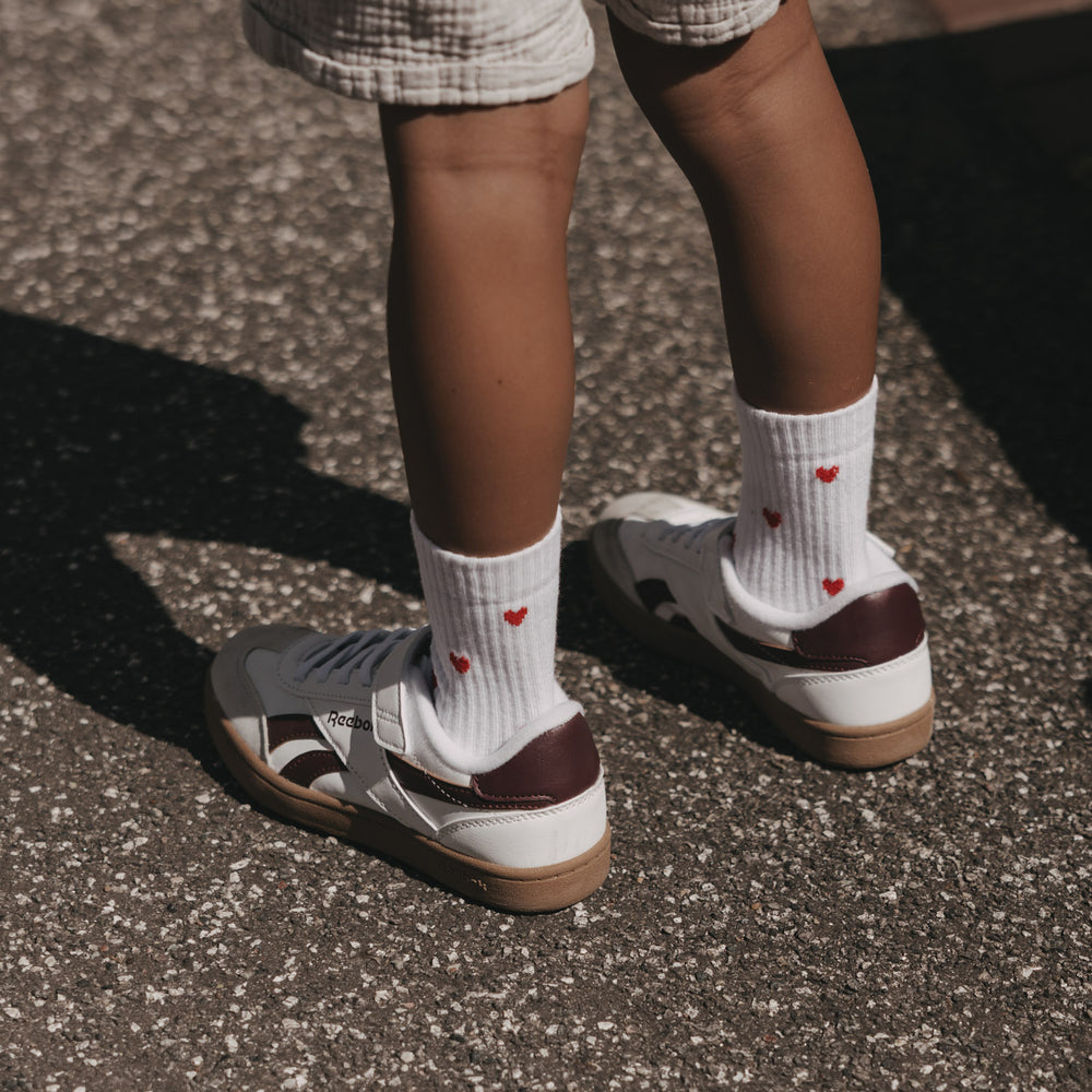 Weiße Eulenschnitt Kindersocken mit roten Herzen, getragen zu hellen Sneakern.