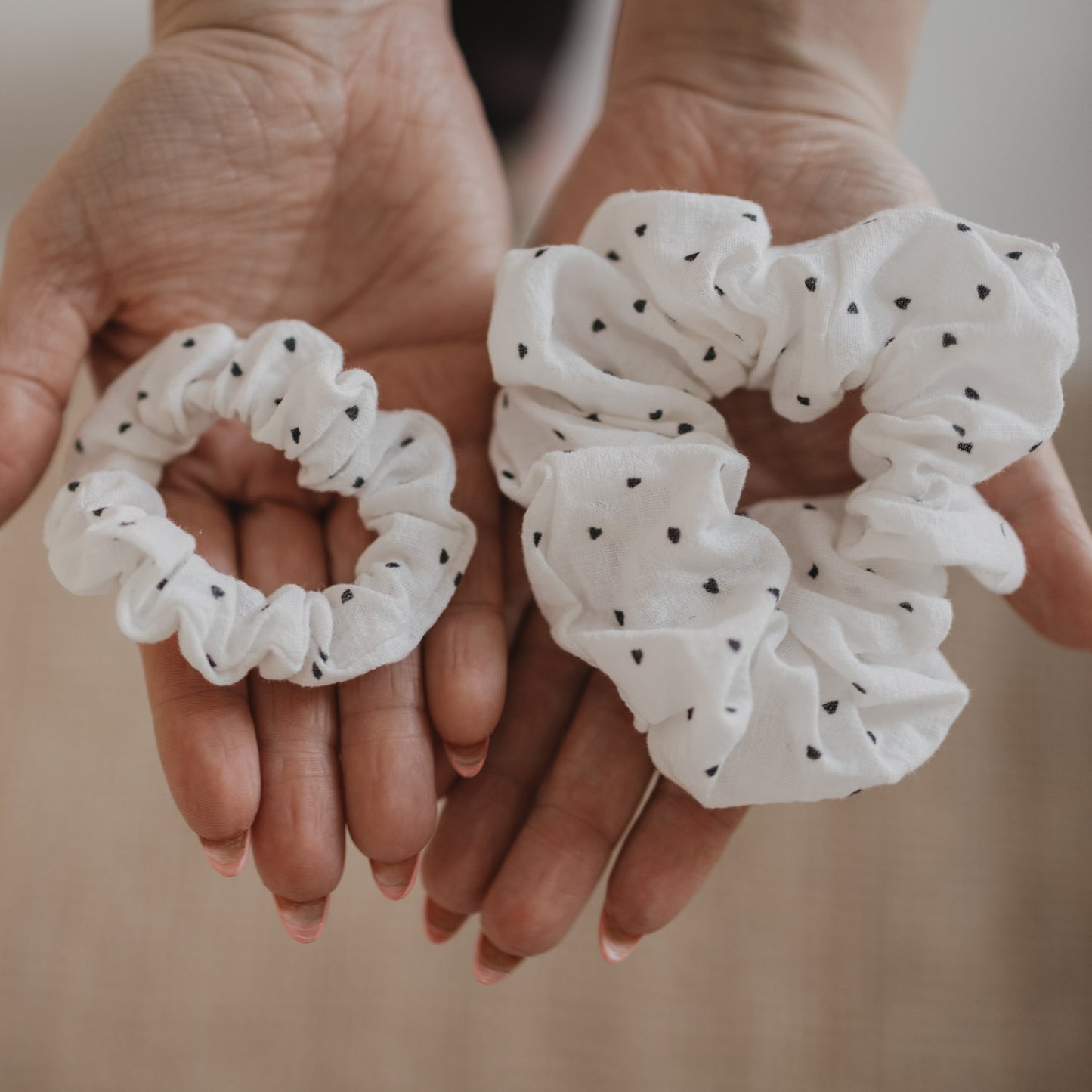 Zwei Scrunchies mit schwarzen Herzen in unterschiedlichen Größen in den Händen präsentiert