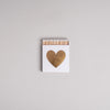Weiße Streichholzschachtel mit goldenem Herz auf hellem Hintergrund – dekorativ und stilvoll.